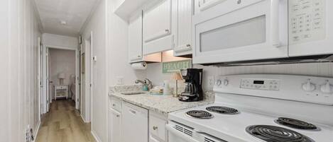 A kitchen with white cabinets, a microwave, a stove, and a coffee maker.