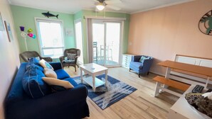 A living room with a blue sofa, a white coffee table, and a wooden bench. - First-Floor, Oceanfront Condo with WiFi & Shared Pools/Hot Tub/Tennis/Game Room (Atlantic Beach)