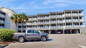 Un hotel de varios pisos con balcones, un área de estacionamiento y una camioneta.