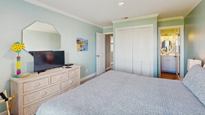 Un dormitorio con cama, cómoda, televisor y puerta que da a un baño.