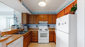 A kitchen with wooden cabinets, a white stove, and a refrigerator. - 2nd Floor in Resort w/Direct Beach Access + Free WiFi, Balcony, Shared Pool (Atlantic Beach)