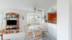 A dining area with a round table, wicker chairs, and a television on a stand. - 2nd Floor in Resort w/Direct Beach Access + Free WiFi, Balcony, Shared Pool (Atlantic Beach)