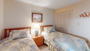 A bedroom with two beds, a nightstand with a lamp, a framed picture on the wall, and a closet with louvered doors. - 2nd Floor in Resort w/Direct Beach Access + Free WiFi, Balcony, Shared Pool (Atlantic Beach)
