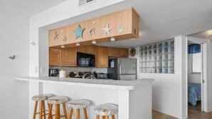 A kitchen with wooden cabinets, a marble countertop, and three bar stools. - Beachfront condo with amazing ocean views, pool, tennis courts, & gym (Atlantic Beach)