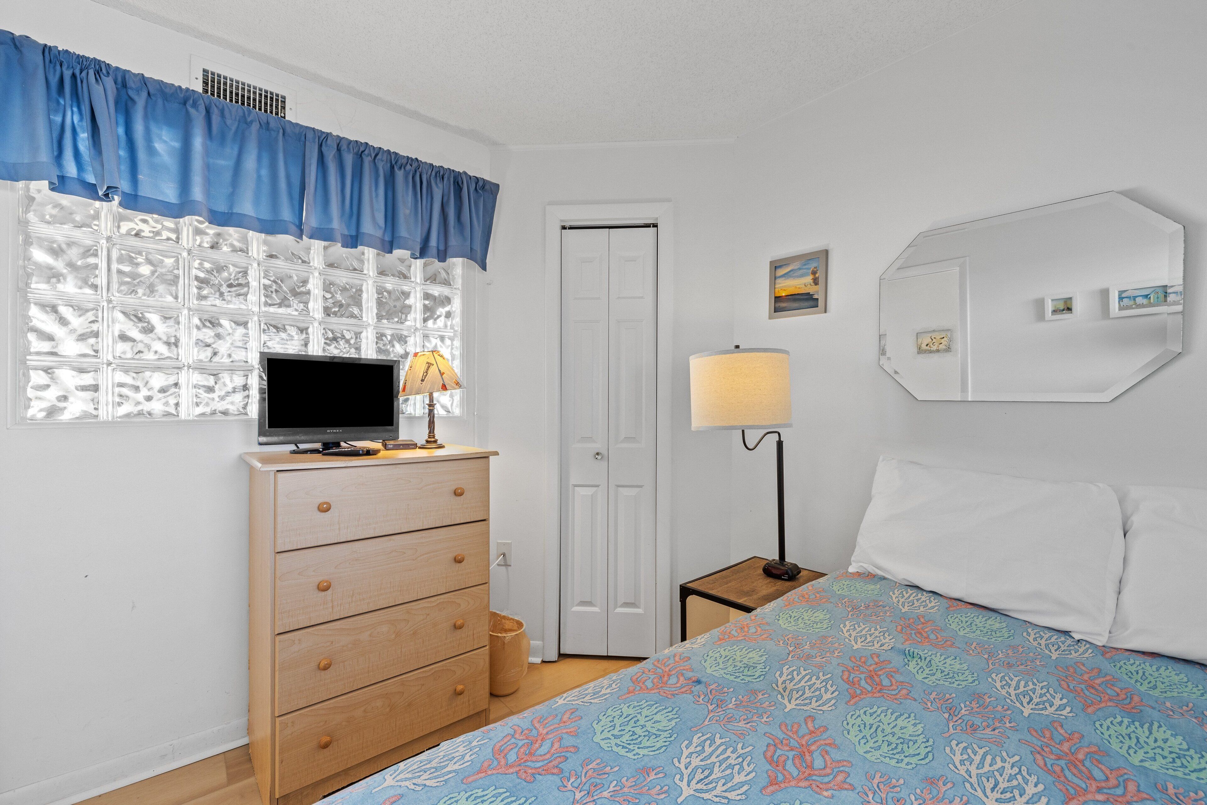 A bedroom with a bed, a dresser, a TV, a lamp, and a window with curtains.