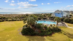 A large house with a swimming pool surrounded by lush greenery and a view of the ocean. - Beachfront condo with amazing ocean views, pool, tennis courts, & gym (Atlantic Beach)