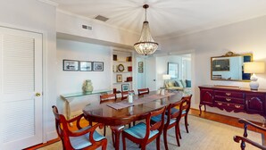 Uma sala de jantar com uma mesa de madeira, cadeiras, um lustre e um espelho na parede.