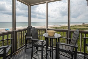Un espacio al aire libre cubierto con vista a la playa, que incluye una mesa con sillas y un cuenco.