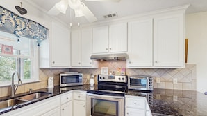 Una cocina moderna con armarios blancos, electrodomésticos de acero inoxidable, encimera de granito y una ventana con un valance decorativo.