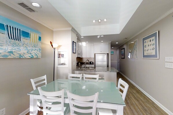 Una cocina moderna con armarios blancos, una isla central y una zona de comedor con mesa de vidrio y sillas blancas.