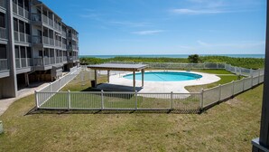 A pool area with a gazebo, surrounded by a white fence, and overlooking a beach. - First-floor, oceanfront condo with great pool view, balconies, WiFi, shared pool (Atlantic Beach)