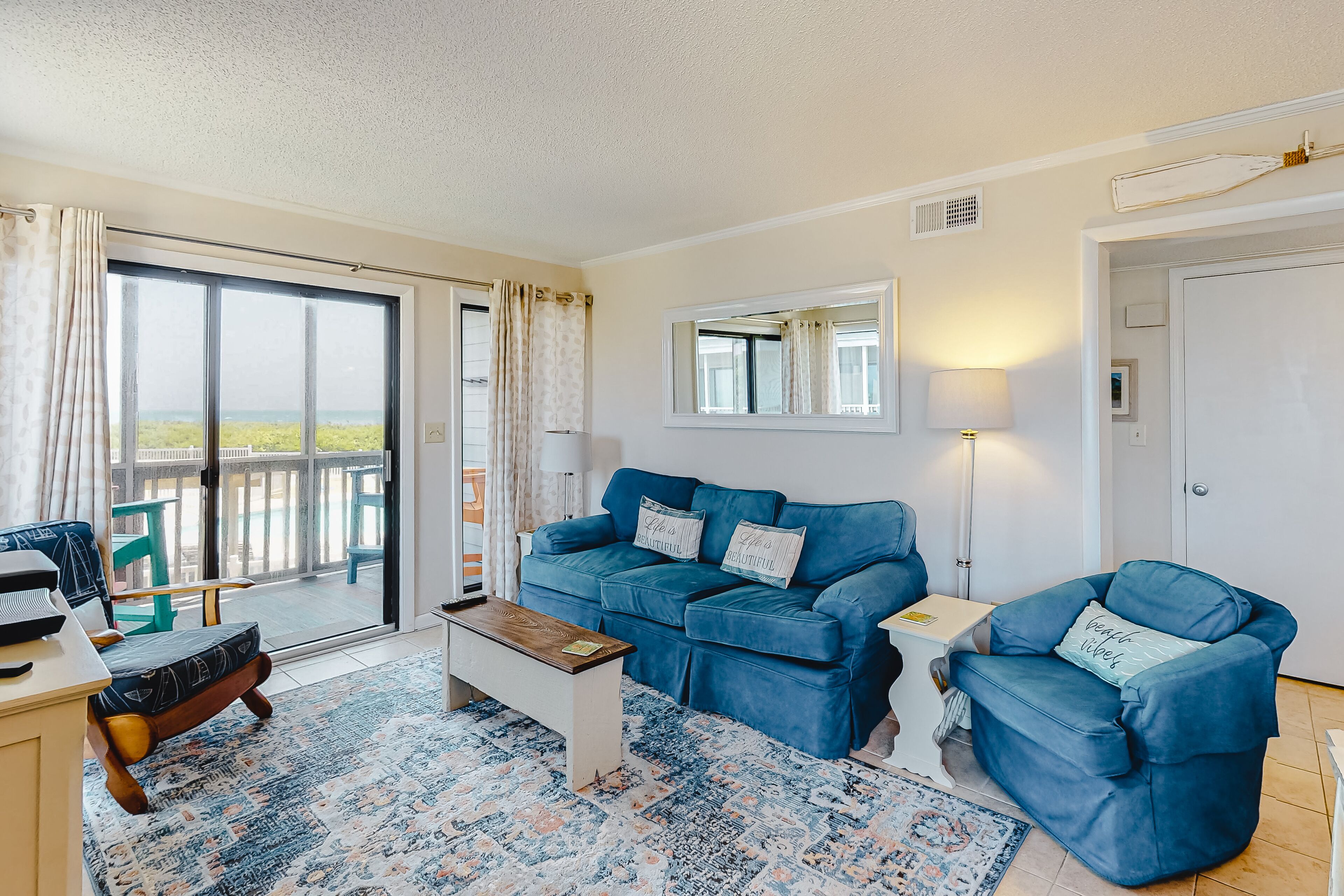 A living room with a blue sofa set, a coffee table, and a view through a sliding glass door.