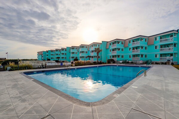 Un edificio turquesa de varios pisos con una piscina delantera.