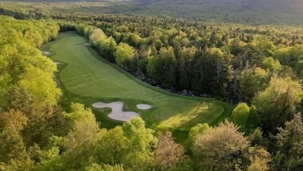 Ein Golfplatz, umgeben von dichtem Wald und Bergen.