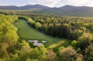A golf course surrounded by dense forest and mountains.