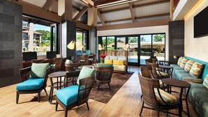 Amplia sala de estar con muebles de mimbre, un sofá y una mesita de centro. Grandes ventanales ofrecen vistas al exterior.