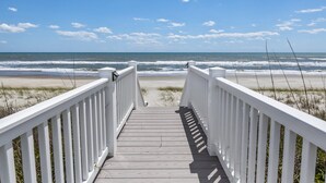 A wooden boardwalk leading to a beach with a clear sky.