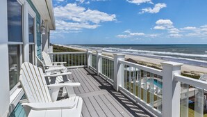A wooden deck with white chairs, a pool, and a view of the beach and ocean.