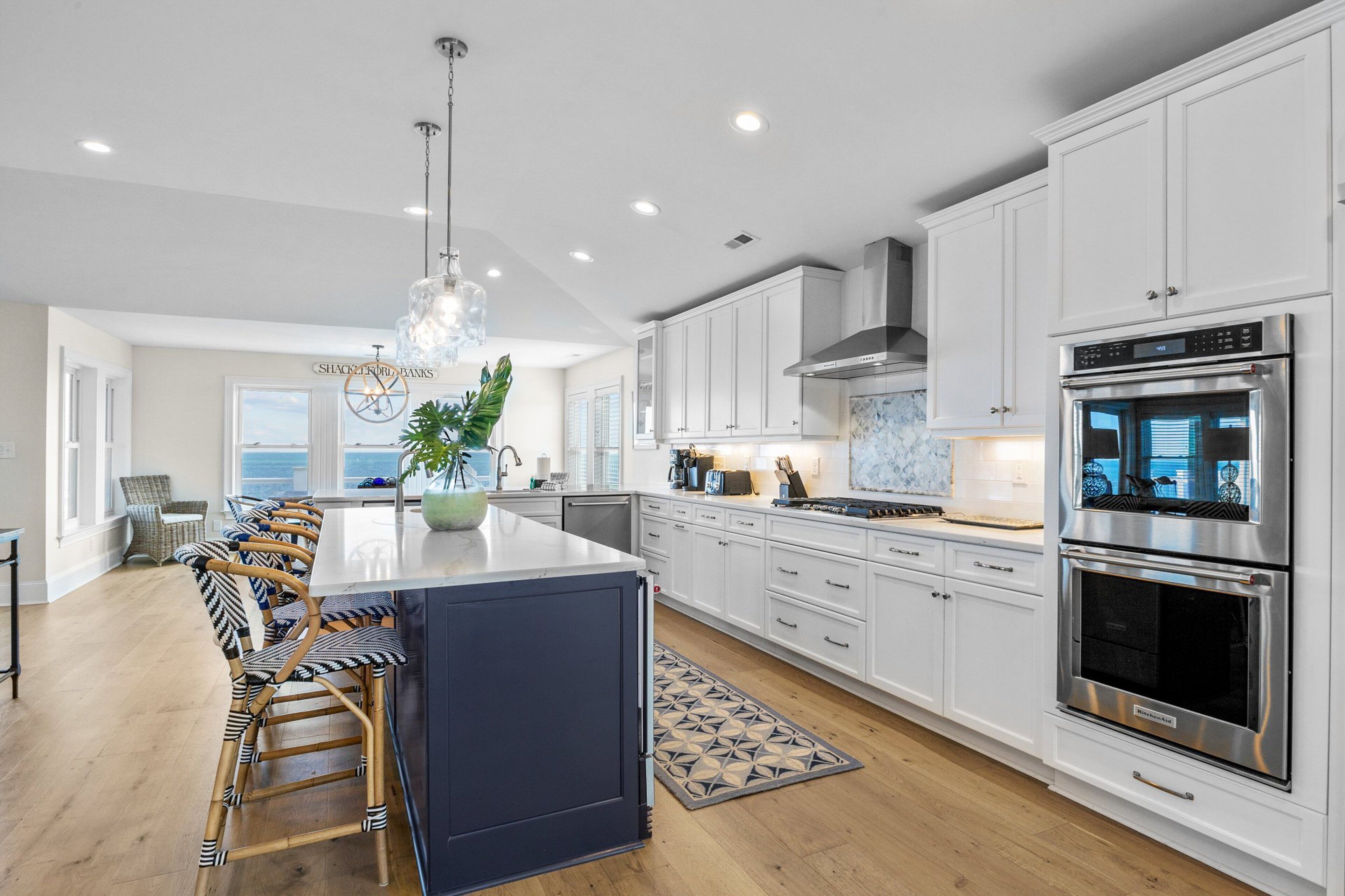 A modern kitchen with white cabinetry, stainless steel appliances, and a large island with bar stools.