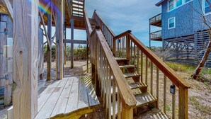 A wooden deck with a staircase leading to a building with a blue exterior. - Oceanfront, Dog-Friendly, 4-Bedroom w/ Private Hot Tub, Ocean View, AC, WiFi (Avon)