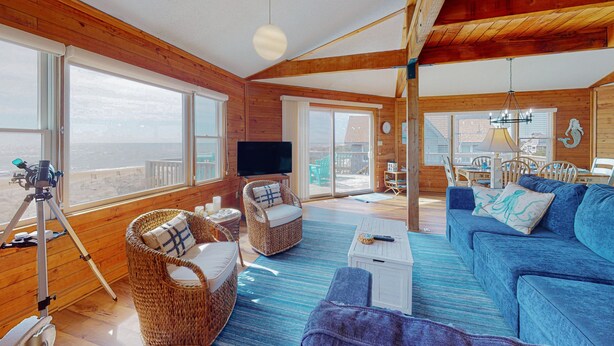 A spacious room with large windows, a blue sofa, wicker chairs, and a telescope on a tripod. - Oceanfront, Dog-Friendly, 4-Bedroom w/ Private Hot Tub, Ocean View, AC, WiFi (Avon)