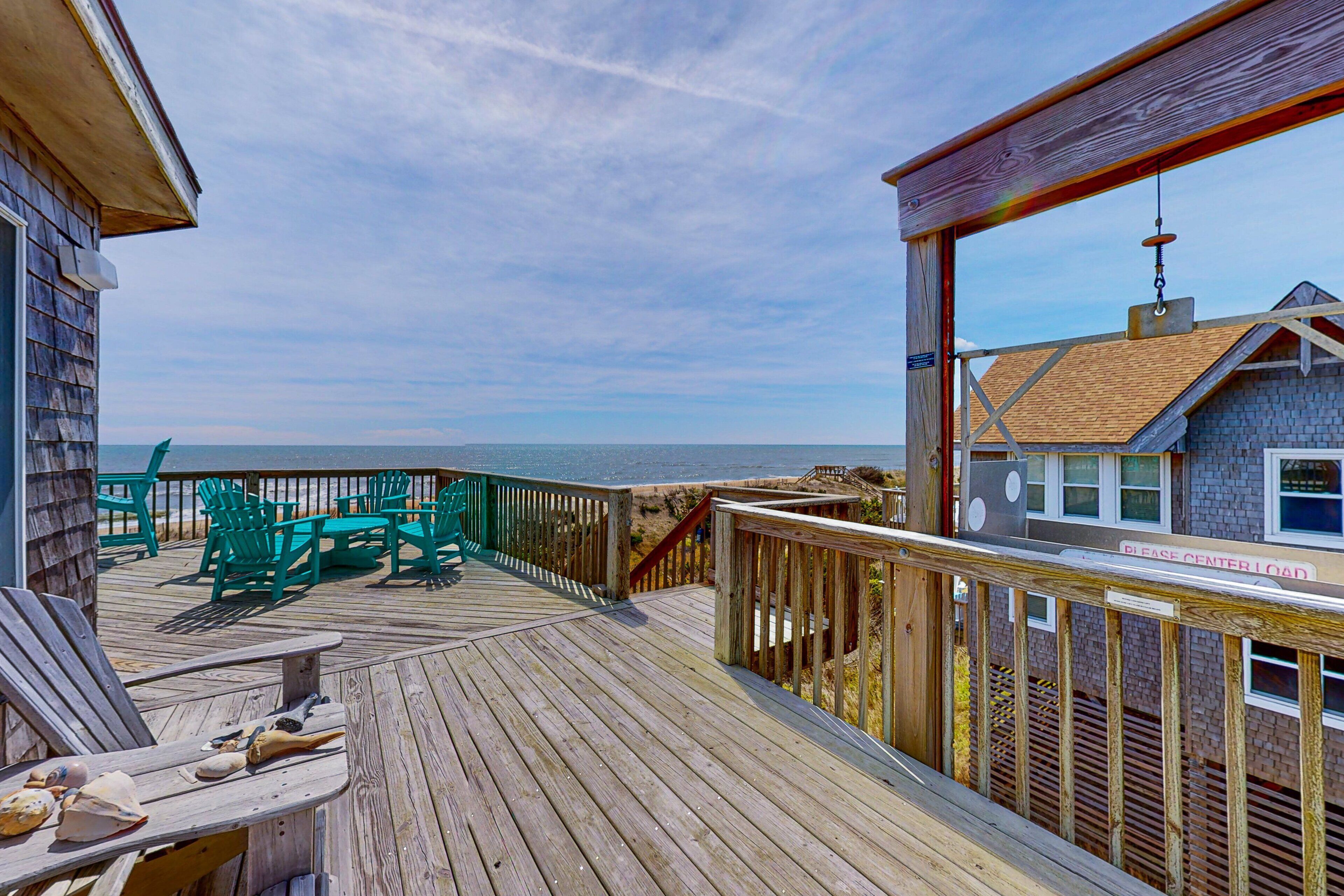 Eine Holzterrasse mit grünen Stühlen und einem Tisch, mit Blick auf den Strand.
