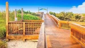 Un pasarelas de madera que conduce a una zona de playa, con un letrero que indica un estacionamiento.
