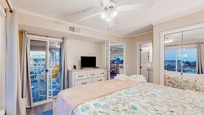 Habitación de hotel con cama, televisor, cómoda, balcón con sillas y vistas a la ciudad.