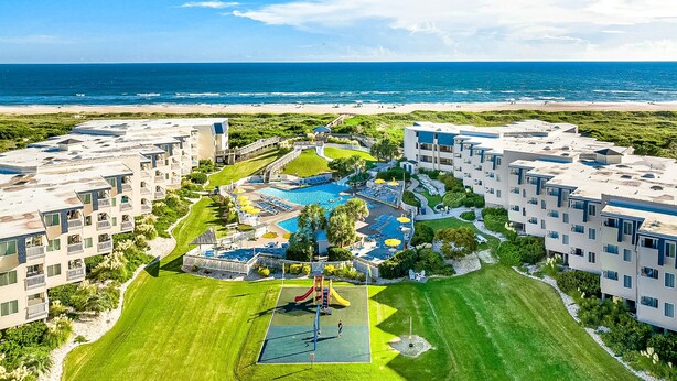 Un resort con varias edificaciones, un área de piscina central y vista a la playa.