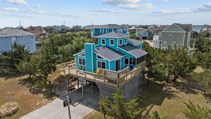 Una casa de varios pisos con terraza, rodeada de árboles y otras viviendas.