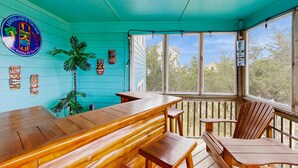 Una terraza de madera con techo turquesa, bancos de madera y un letrero de bar tiki.