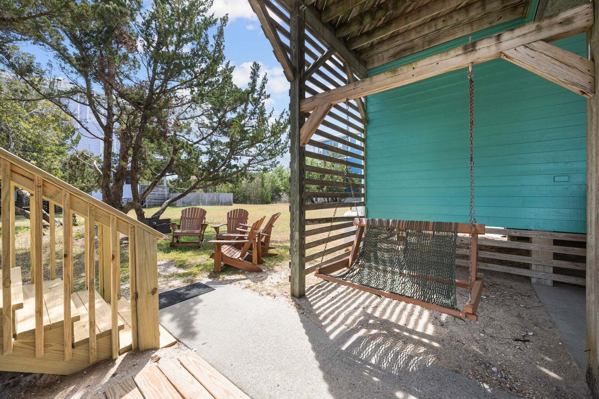 A wooden deck with chairs, a swing, and a green building in the background.