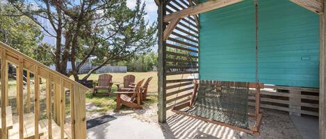 A wooden deck with chairs, a swing, and a green building in the background.