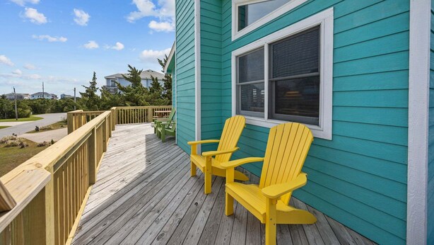 Una casa turquesa con una terraza de madera y dos sillas Adirondack amarillas.