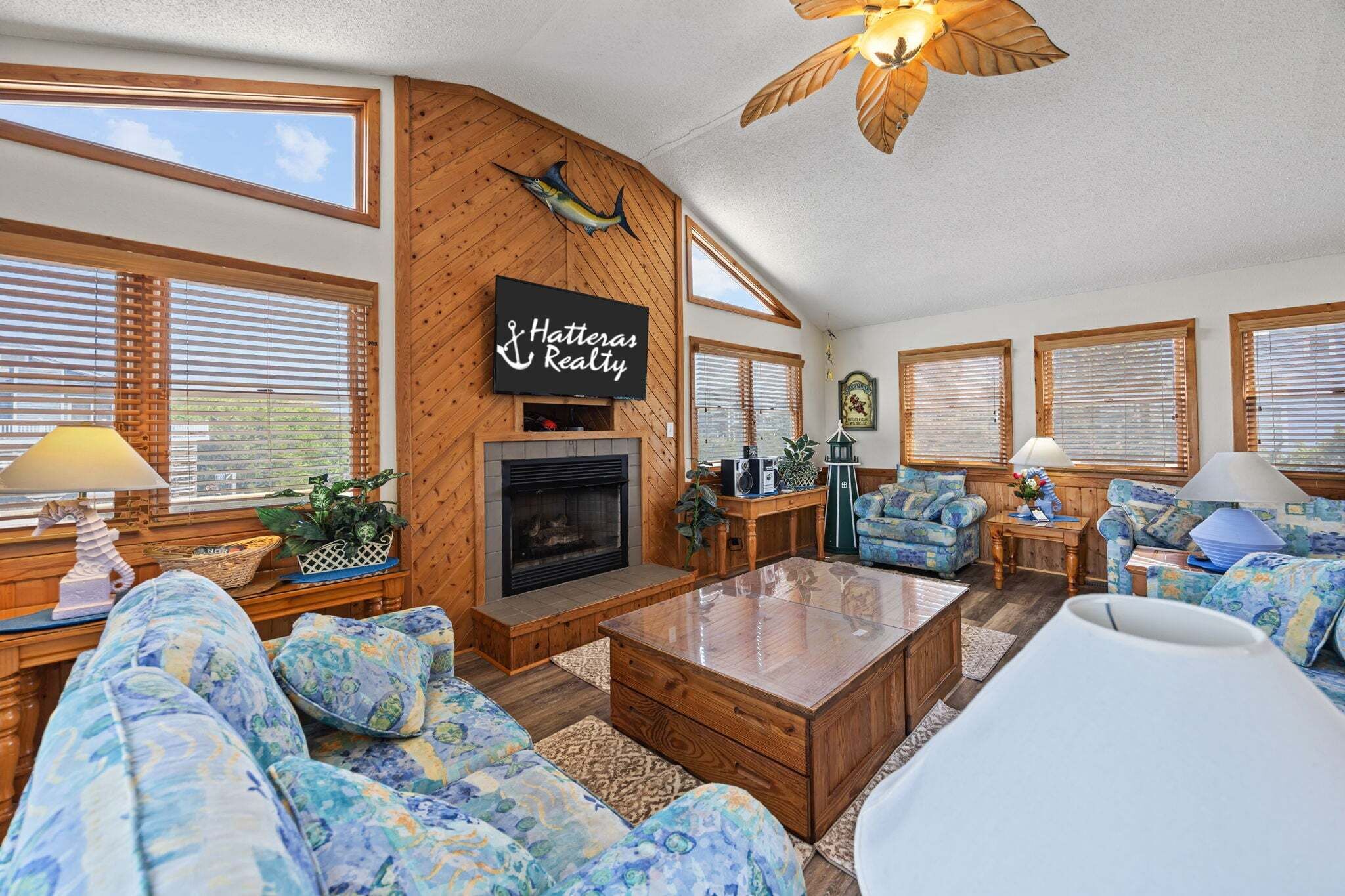 A cozy living room with a fireplace, wooden walls, and blue patterned furniture.