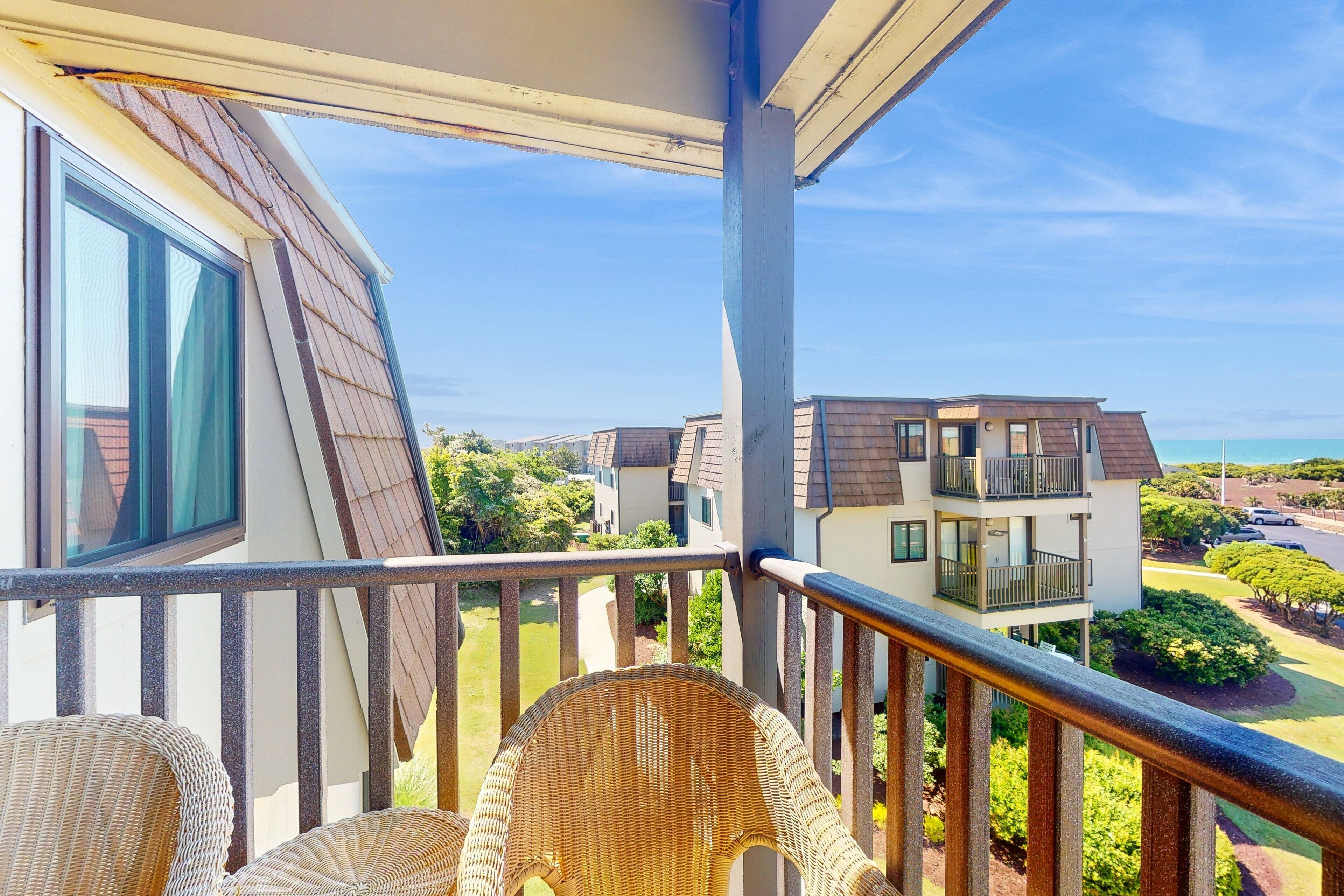 A balcony with wicker chairs, a view of neighboring houses, and a clear sky.