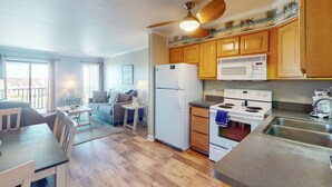 Una cocina moderna con armarios de madera, un refrigerador, un microondas y una estufa. Hay un comedor con mesa y sillas, y un ventilador de techo arriba.
