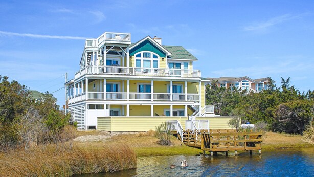 A multi-story waterfront property with balconies, a dock, and a pond with ducks.