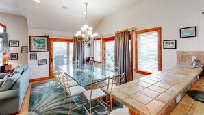 A spacious living area with a glass dining table, comfortable seating, and a large window with curtains.