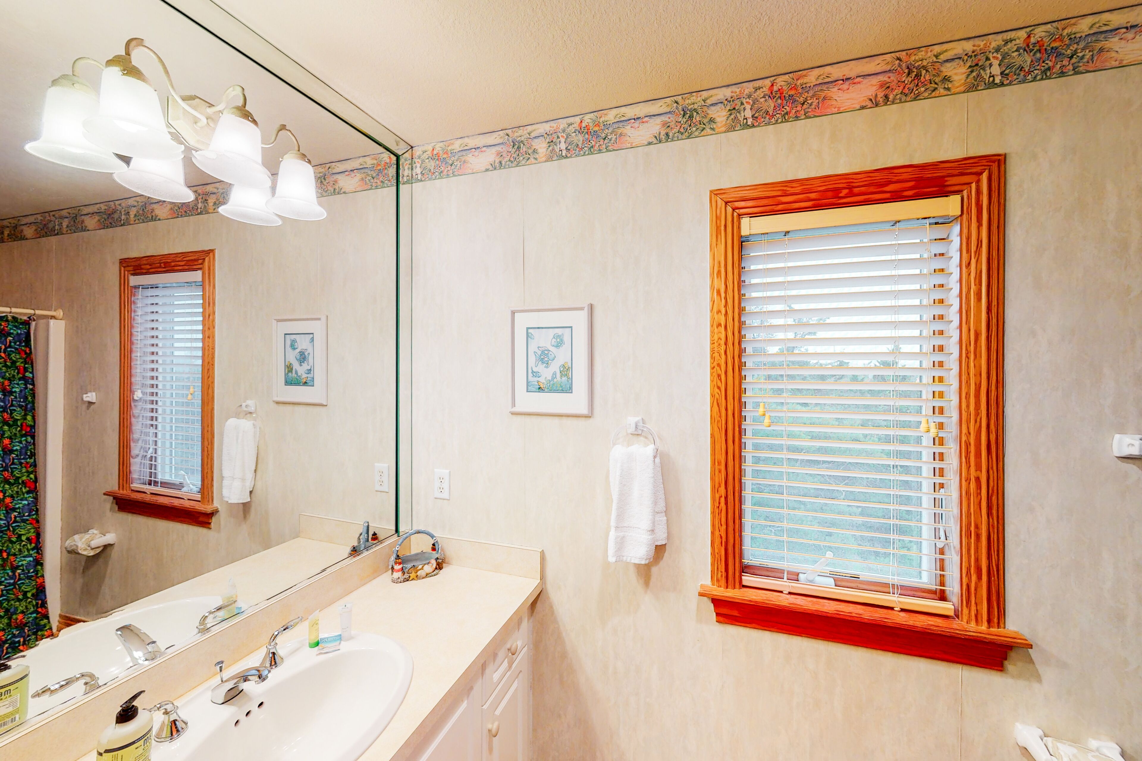 Une salle de bain avec un grand miroir, un lavabo et une fenêtre avec des stores.