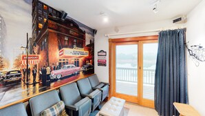 A hotel room with a large mural of a vintage car and city scene, a balcony with a view, and a seating area with a small table and chairs.