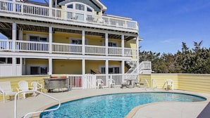 A two-story building with a swimming pool, outdoor seating, and a white railing.