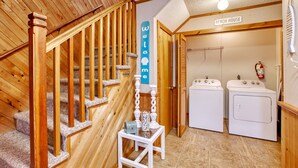 Un escalier en bois mène à une buanderie où l’on peut voir une pancarte « Bienvenue » et, au-dessus de la porte, une autre pancarte indiquant « Maison de plage ».