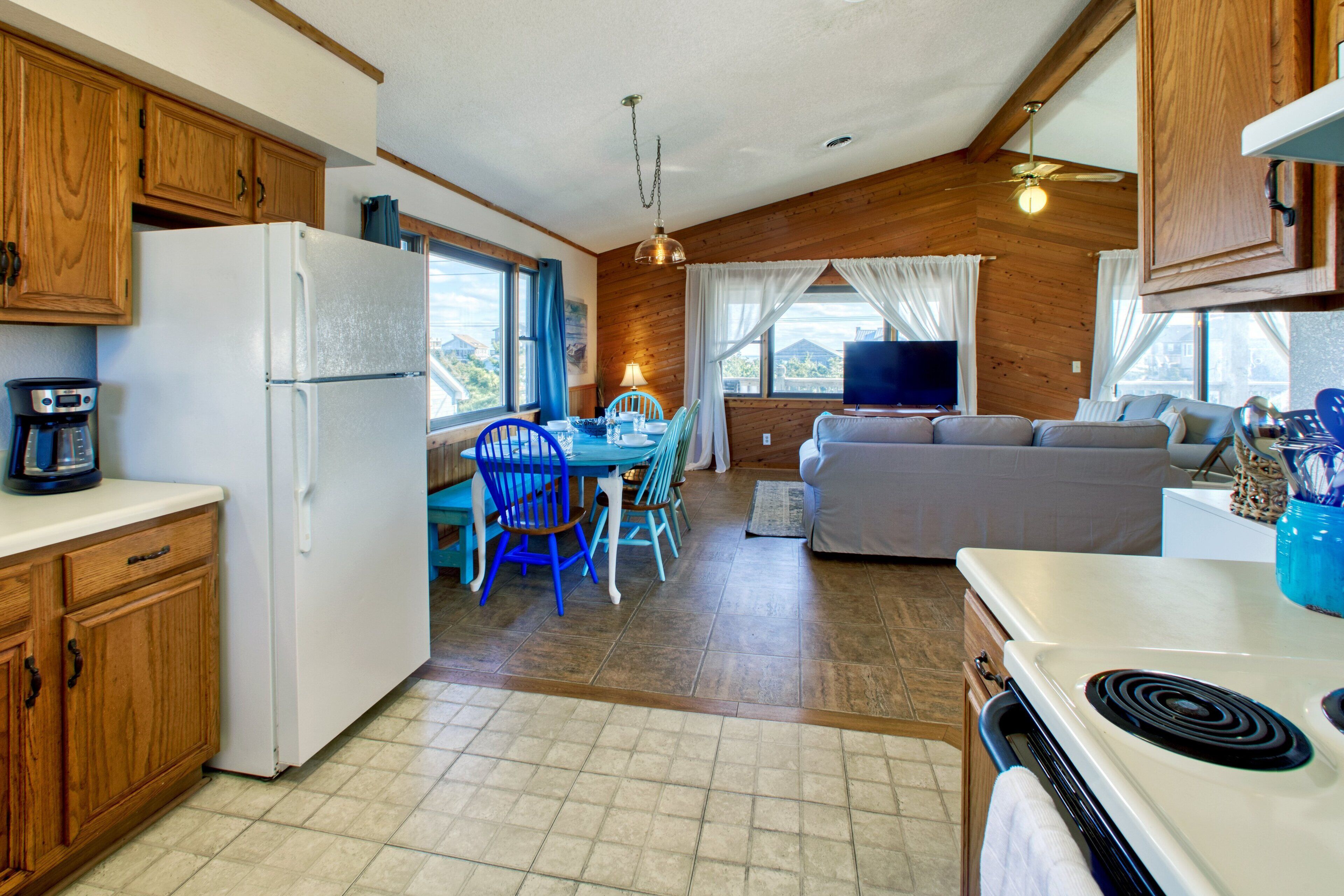 A compact kitchen with a refrigerator, stove, and dining area with blue chairs.