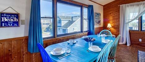 Un coin repas avec une table en bois et des chaises bleues, une fenêtre avec des rideaux bleus et un panneau accroché au mur.