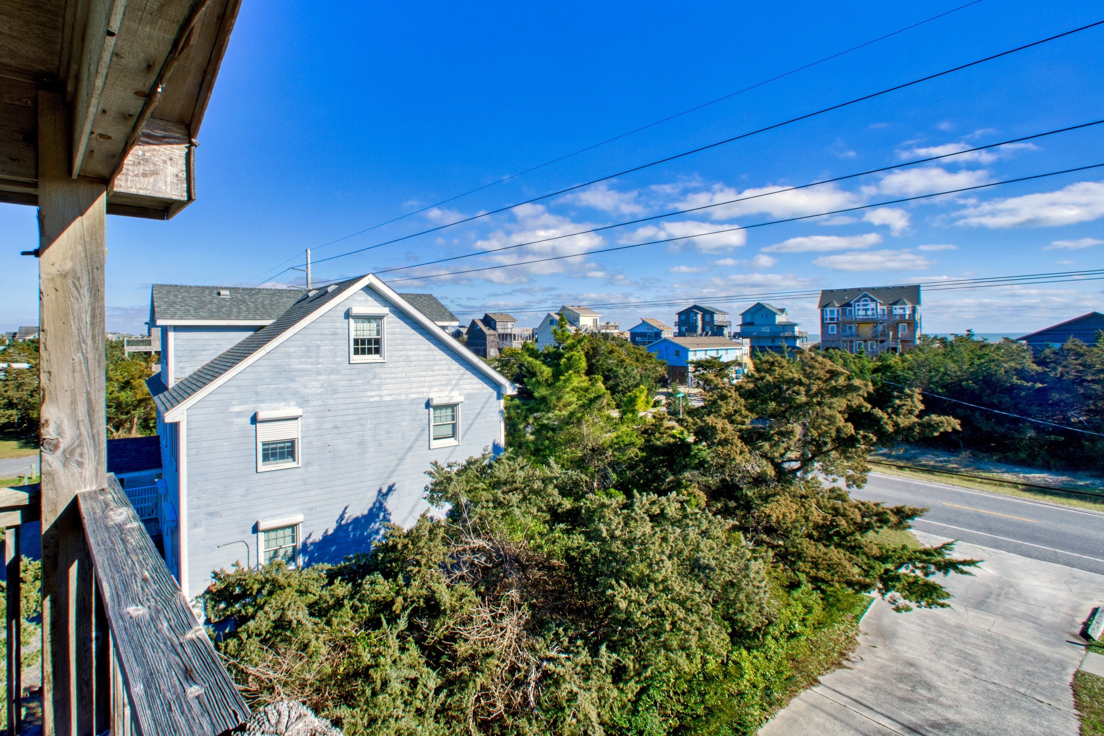 A coastal house with a sloped roof, surrounded by dense greenery and a clear blue sky.