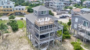 A multi-story beachfront property with a deck, outdoor seating, and a sandy beach area. - Gray Haven #11-DE: Oceanfront, dog-friendly, private hot tub, pool access (Avon)