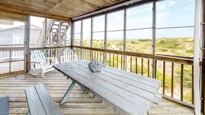 A wooden deck with a table and chairs, overlooking a beach with dunes and a house in the background. - Gray Haven #11-DE: Oceanfront, dog-friendly, private hot tub, pool access (Avon)