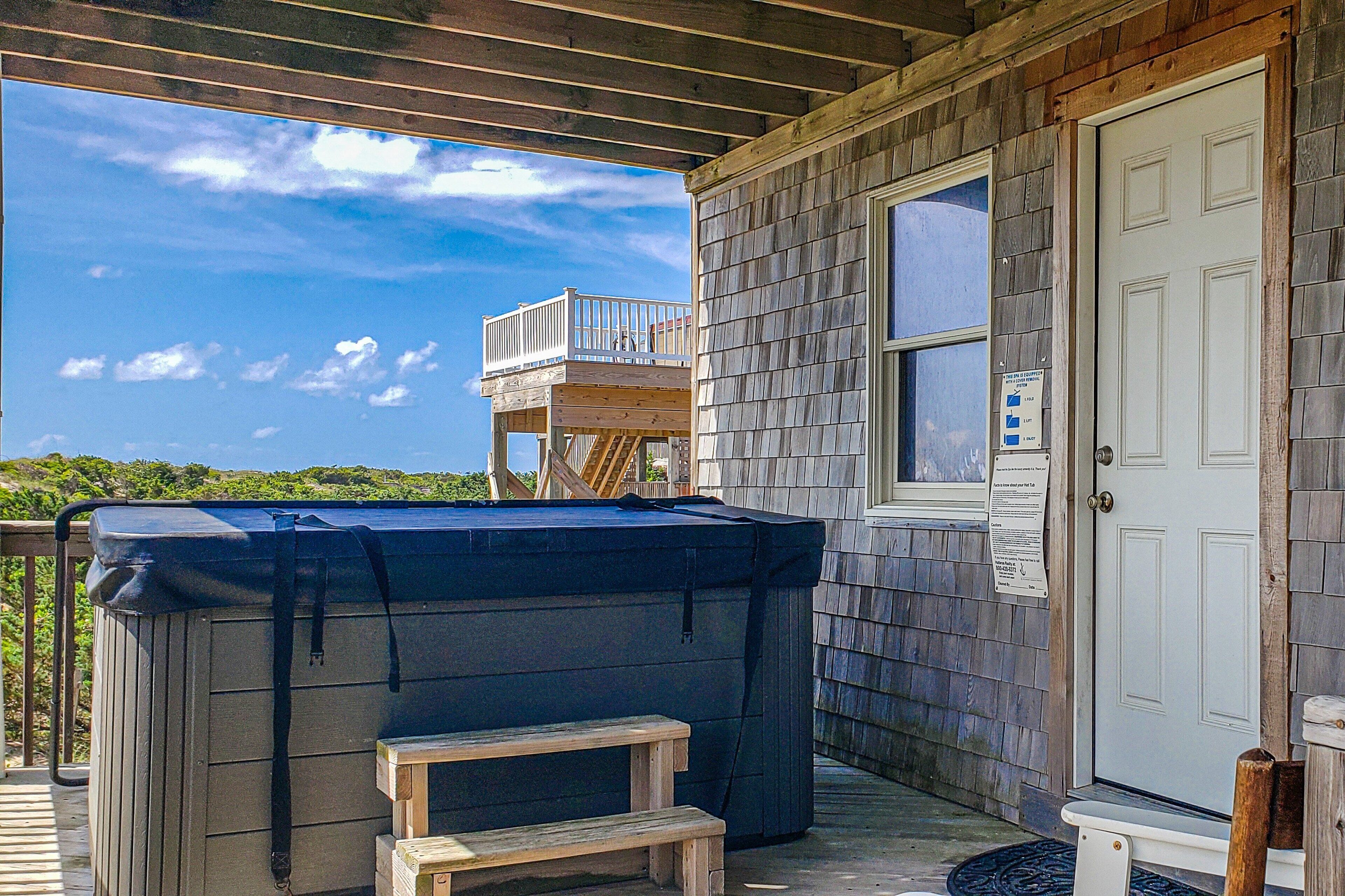 A covered deck with a hot tub, a small wooden stool, and a door with a window.