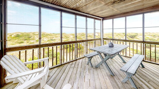 A covered deck with a wooden floor and a table with benches. - Gray Haven #11-DE: Oceanfront, dog-friendly, private hot tub, pool access (Avon)